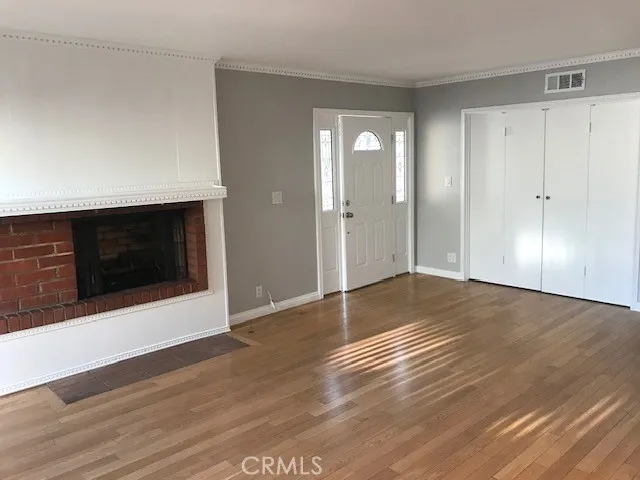 a view of an empty room with wooden floor and a kitchen