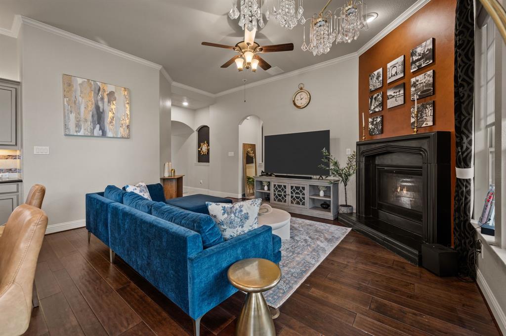 616 Whitetail Road Euless, TX 76039 - Photo 9 of 39 Living area featuring ornamental molding, a glass covered fireplace, dark wood-style flooring, arched walkways, and a ceiling fan
