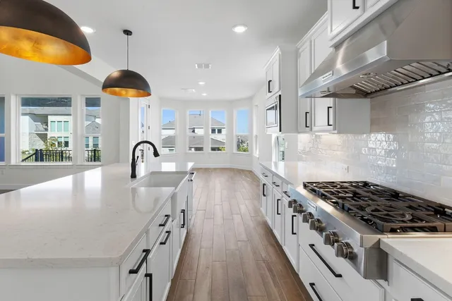 a kitchen with stainless steel appliances granite countertop a stove a sink dishwasher and white cabinets with wooden floor