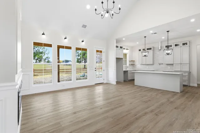 a view of an empty room with wooden floor and a kitchen
