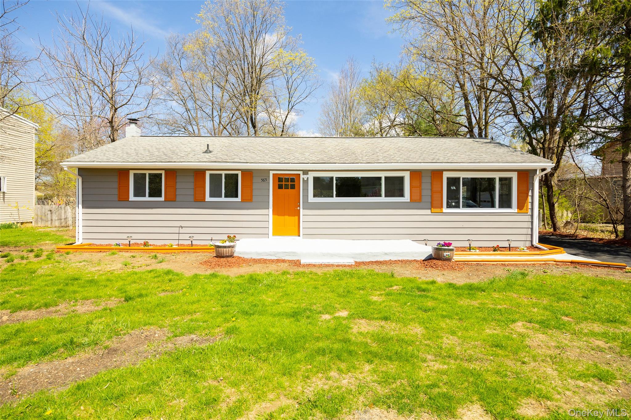 Single story home featuring a front lawn, a chimney, roof with shingles, and a patio