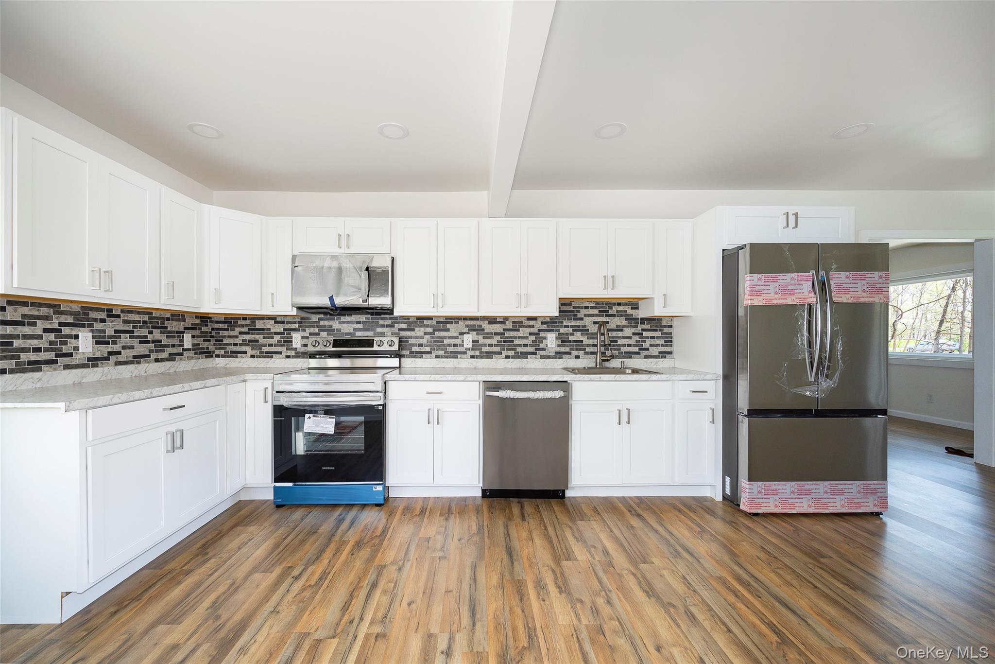 565 Old Hopewell Road Hopewell Junction, NY 12533 - Photo 3 of 23 Kitchen with appliances with stainless steel finishes, white cabinets, dark wood-type flooring, light stone counters, and beamed ceiling