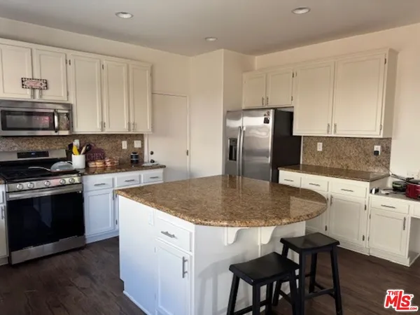 a kitchen with stainless steel appliances granite countertop a stove top oven a refrigerator a sink and white cabinets