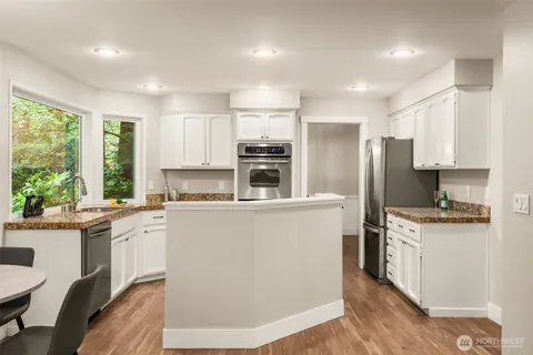 a kitchen with stainless steel appliances granite countertop a refrigerator a sink dishwasher a stove and white cabinets with wooden floor