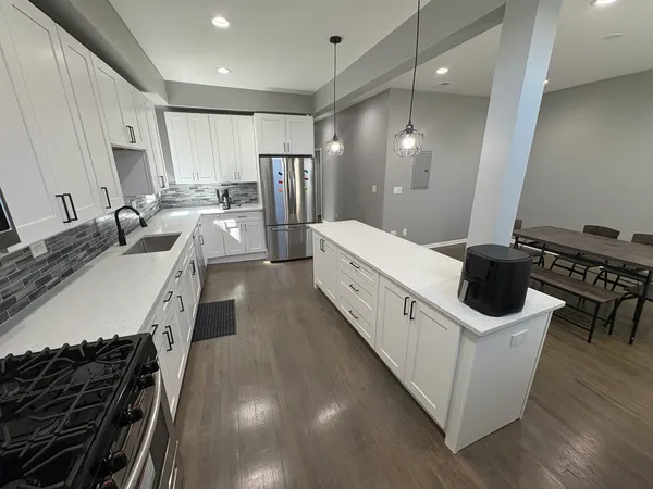 a large white kitchen with a stove a sink a refrigerator and a dining table with wooden floor