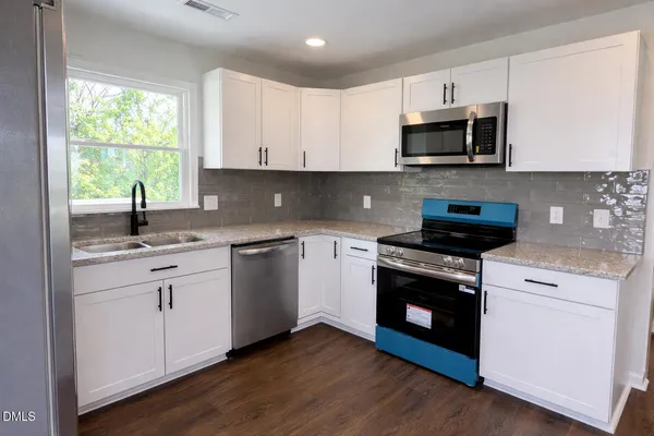 a kitchen with stainless steel appliances granite countertop white cabinets a sink and a window