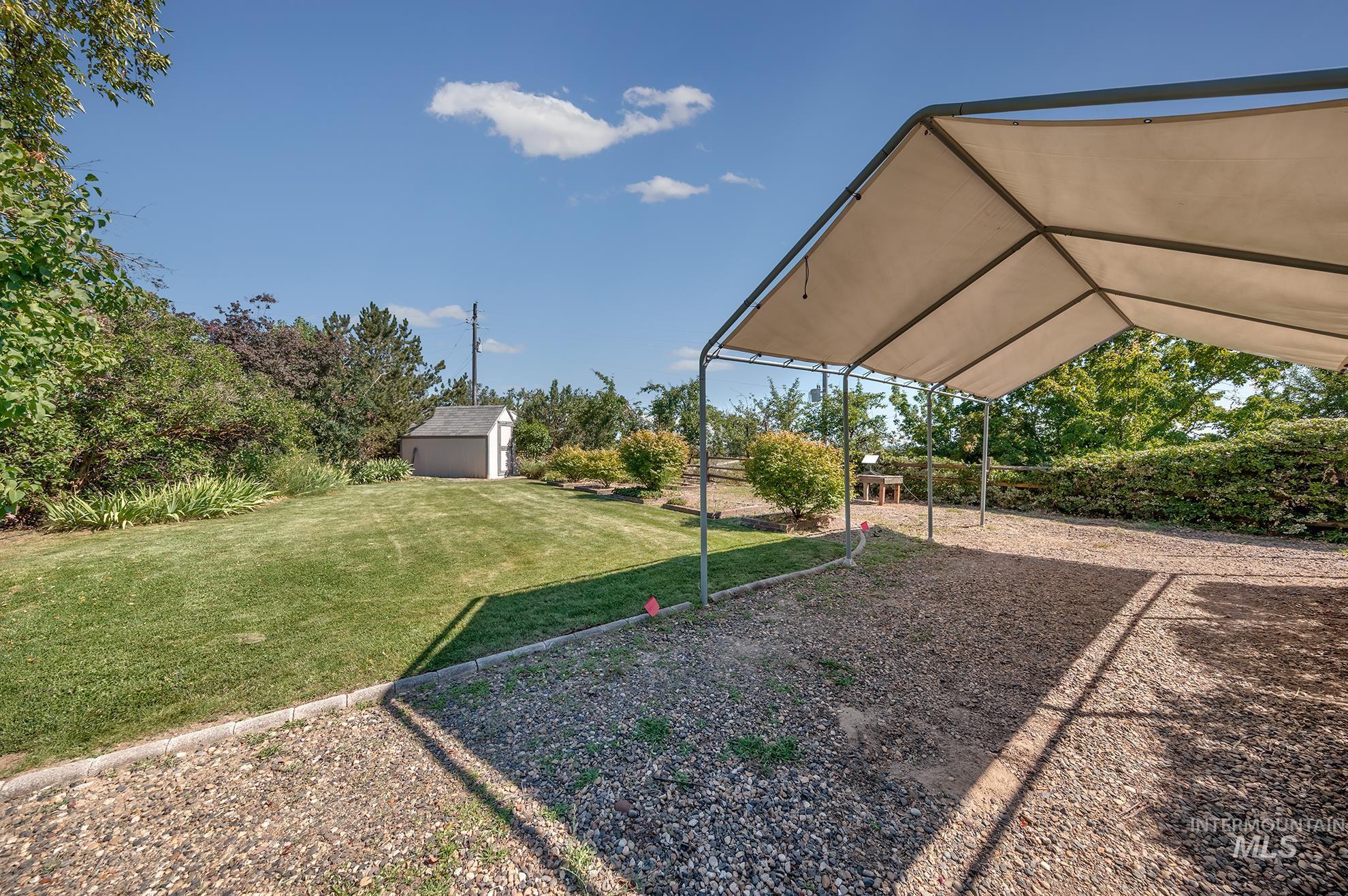 1493 Cove Road Weiser, ID 83672 - Photo 44 of 50 Spacious exterior featuring a gravel area with a metal-frame canopy, a manicured lawn, a detached storage shed, lush shrubbery, and mature trees