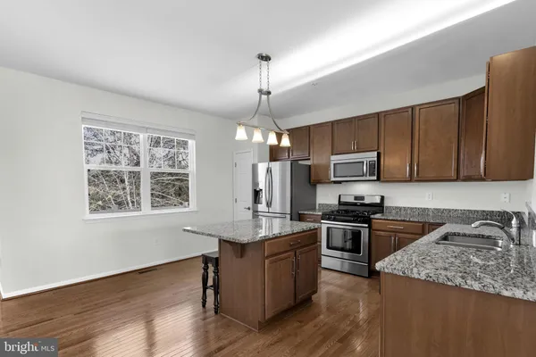 a kitchen with stainless steel appliances granite countertop a stove a sink dishwasher a refrigerator and a microwave oven with wooden floor