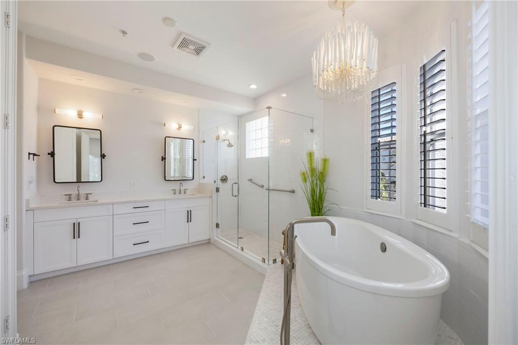 2870 Castillo Court, Unit 103 Naples, FL 34109 - Photo 13 of 34 a large white bathroom with a bathtub a mirror a sink and vanity