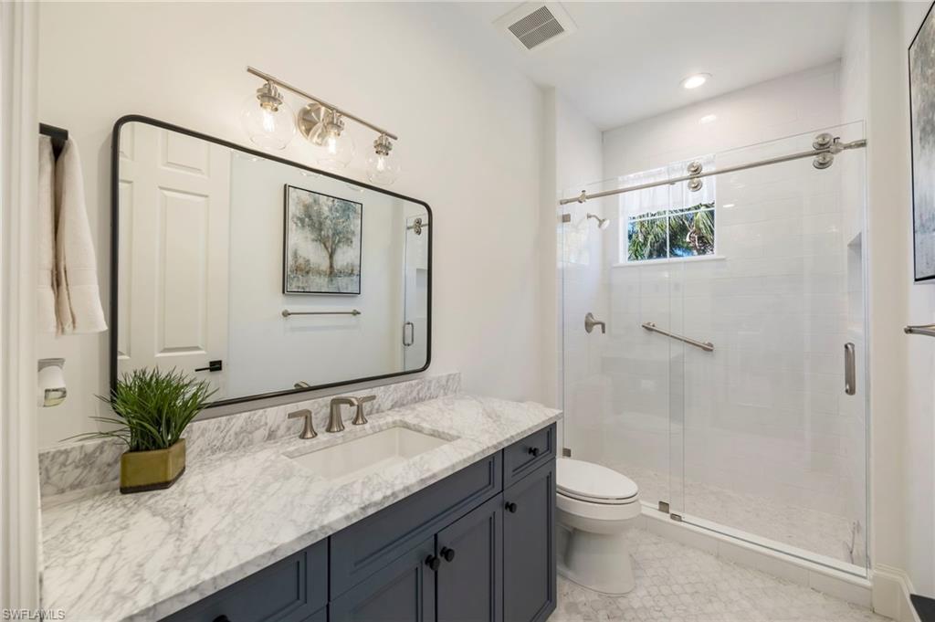 2870 Castillo Court, Unit 103 Naples, FL 34109 - Photo 18 of 34 a bathroom with a granite countertop sink a toilet a large mirror and shower