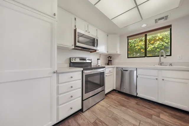 a kitchen with white cabinets appliances a sink and a window