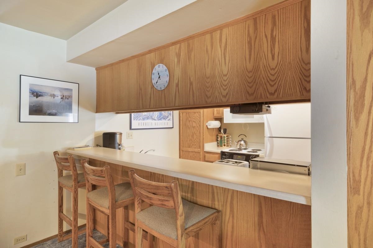 244 Lakeview Boulevard, Unit 149 Mammoth Lakes, CA 93546 - Photo 14 of 29 Kitchen with a breakfast bar area, light countertops, brown cabinets, stove, and freestanding refrigerator