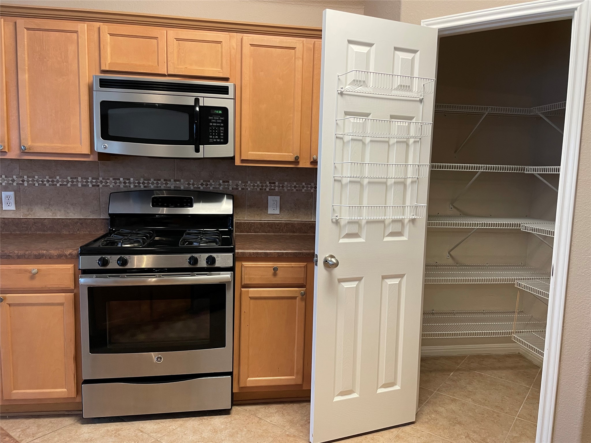 11713 Dunblane Way Austin, TX 78754 - Photo 6 of 22 Kitchen featuring stainless steel range and microwave, wood cabinetry, patterned tile backsplash, and a walk-in pantry with wire shelving