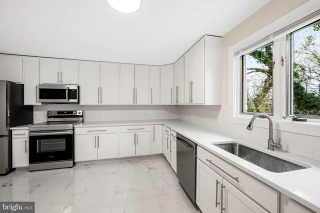 a kitchen with white cabinets appliances a sink and a window