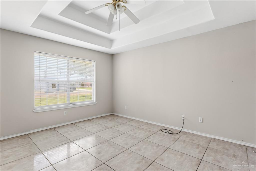 402 Mockingbird Lane Edcouch, TX 78538 - Photo 13 of 25 Spacious room featuring a decorative tray ceiling with a ceiling fan, a large window with horizontal blinds, and tiled flooring