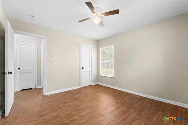 an empty room with wooden floor fan and windows