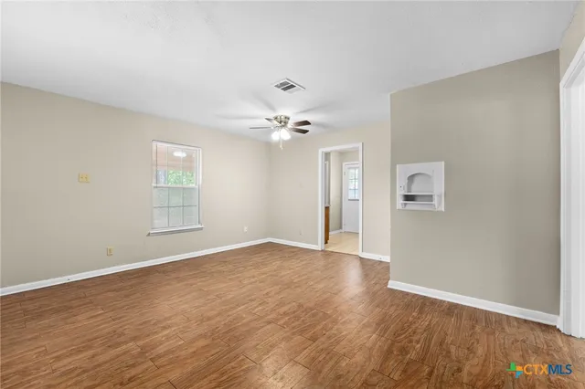 a view of an empty room with wooden floor and a ceiling fan
