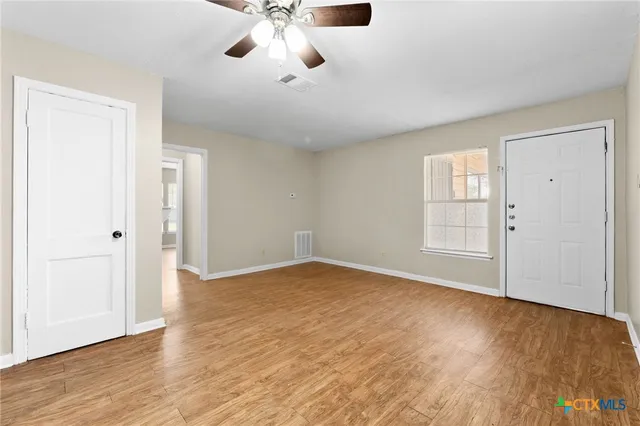 an empty room with wooden floor chandelier fan and windows