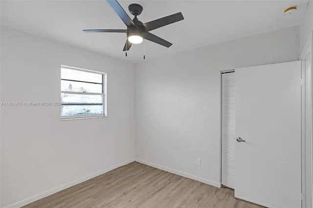 an empty room with wooden floor chandelier fan and windows