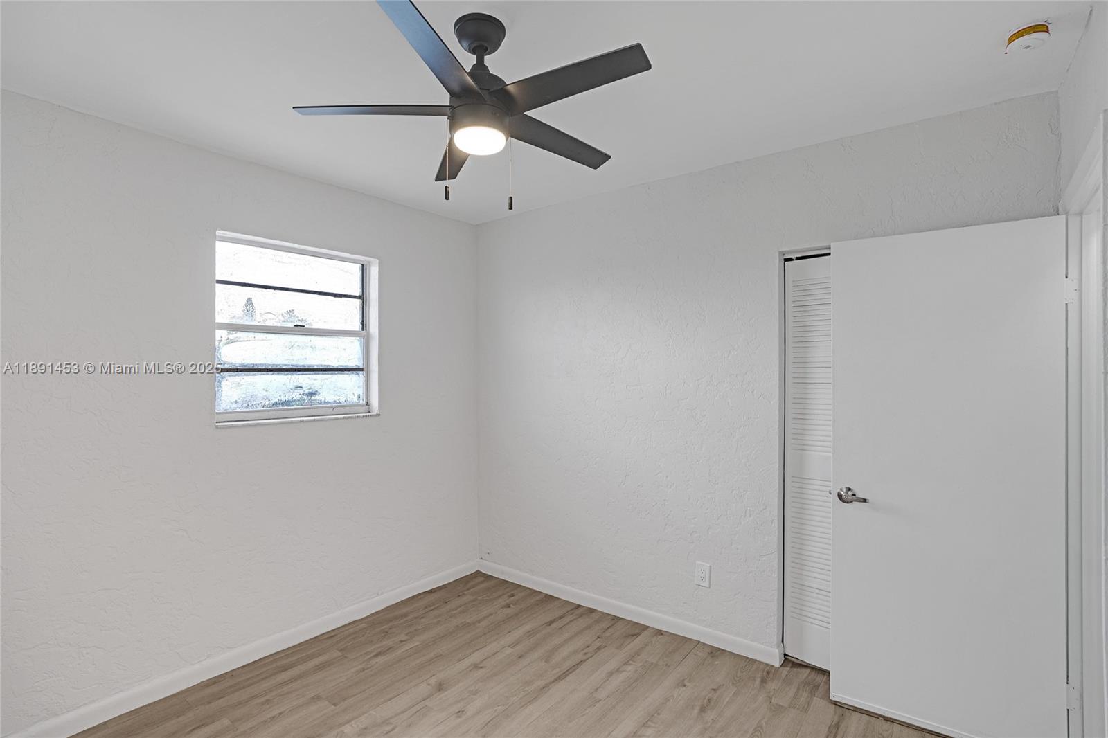 14100 Northwest 24th Court, Unit 303 Opa-Locka, FL 33054 - Photo 14 of 21 an empty room with wooden floor chandelier fan and windows