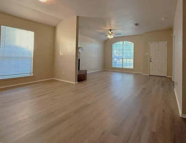 an empty room with wooden floor chandelier and windows
