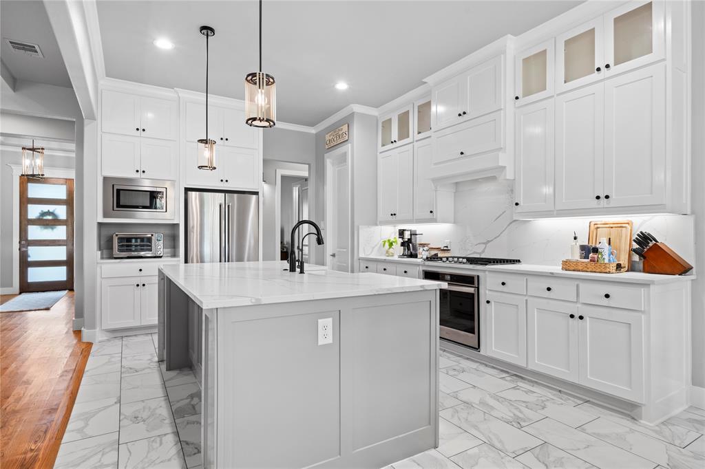 1024 Henry Way Springtown, TX 76082 - Photo 13 of 29 Modern kitchen featuring a central island with a waterfall-edge countertop, stainless steel appliances, white shaker cabinetry, and marble-look tile flooring