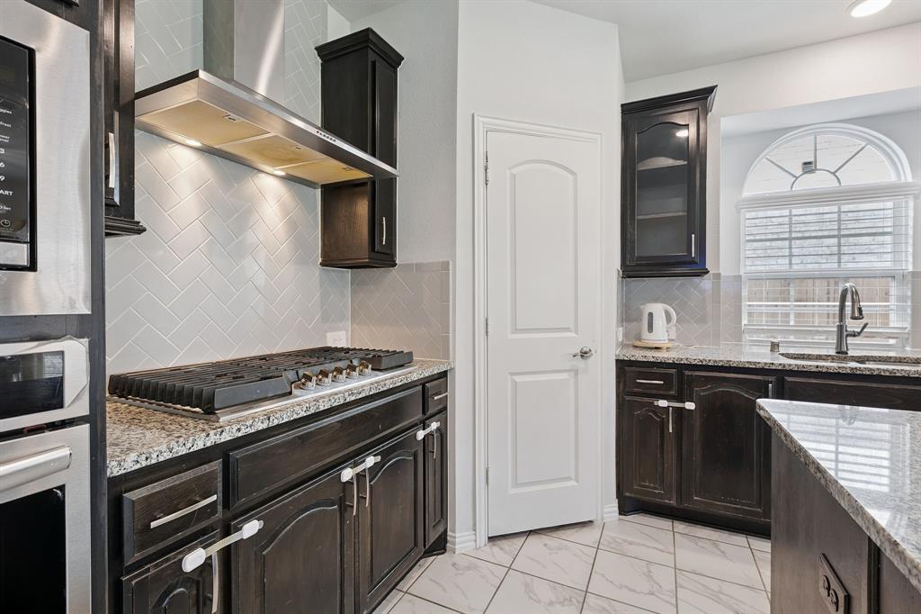 Undisclosed Address Wylie, TX 75098 - Photo 11 of 26 Kitchen with wall chimney range hood, stainless steel appliances, light marble finish flooring, tasteful backsplash, and light stone counters