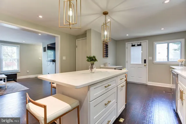 a hall with kitchen island white cabinets and wooden floor