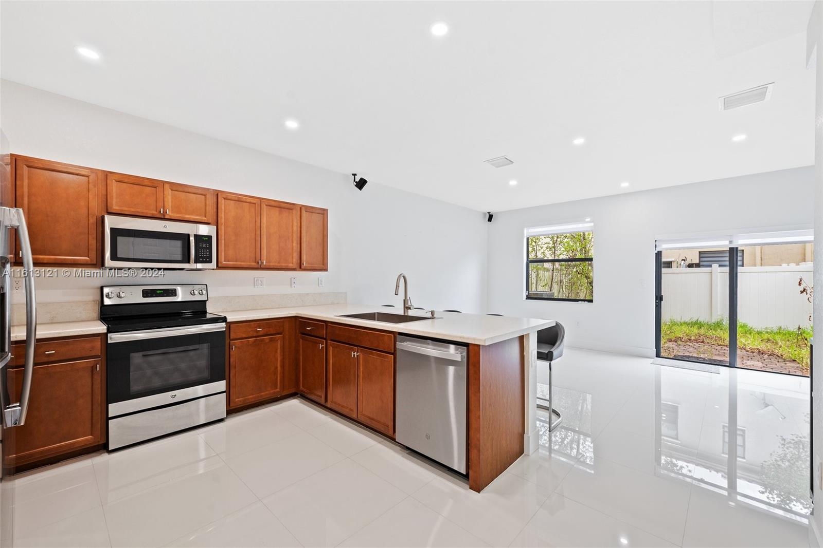 9361 West 33rd Way Hialeah, FL 33018 - Photo 6 of 30 a kitchen with stainless steel appliances granite countertop a stove top oven a sink dishwasher a dining table and chairs with wooden floor