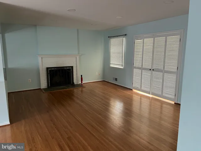 an empty room with wooden floor fireplace and windows