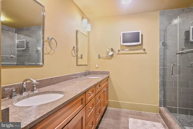 a bathroom with a granite countertop double vanity sink a mirror and a shower