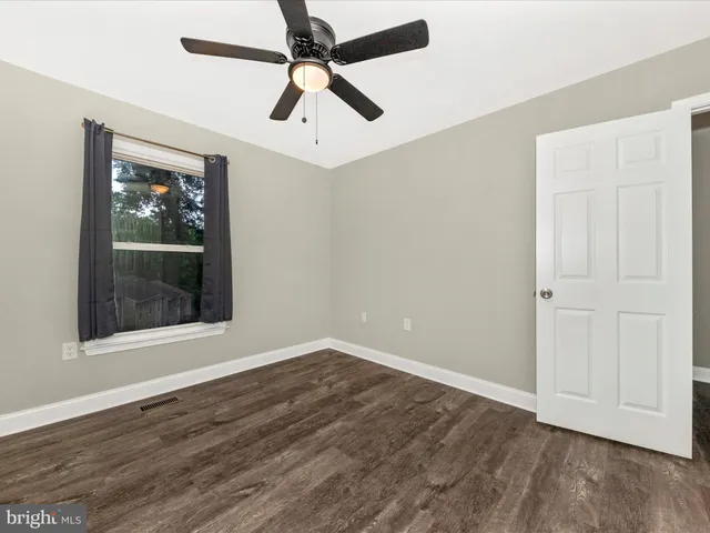 an empty room with wooden floor ceiling fan and windows