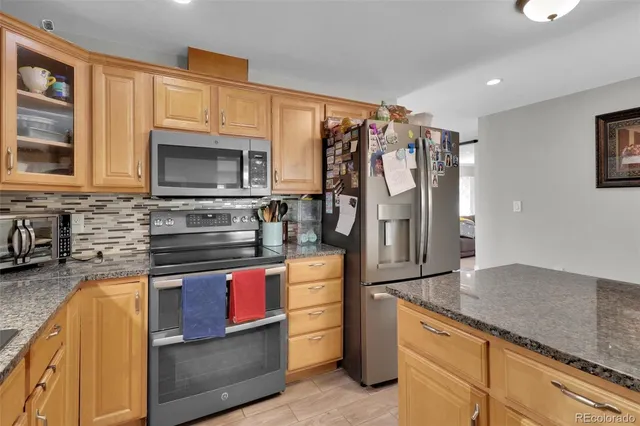 a kitchen with stainless steel appliances granite countertop a refrigerator a stove top oven and a sink with wooden floor