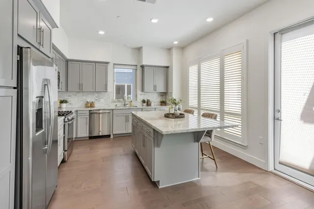 a kitchen with stainless steel appliances granite countertop a refrigerator a sink a stove a dining table and chairs