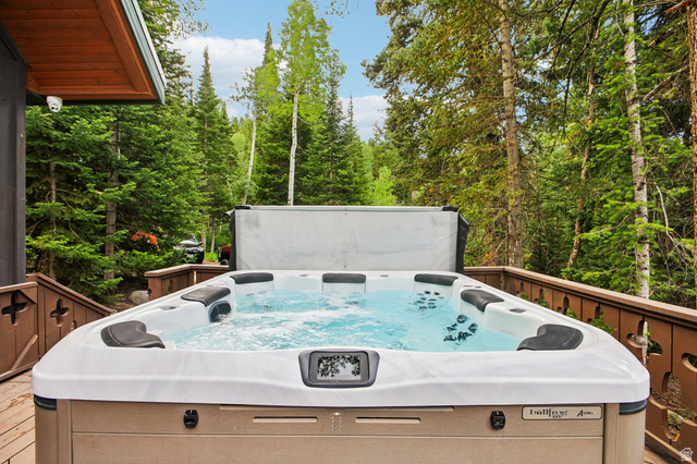 10205 East Moose Loop Road Salt Lake City, UT 84121 - Photo 37 of 50 Outdoor spa featuring bubbling water, multiple seating areas, a built-in cover, and a surrounding wood deck with a decorative railing, all set amidst mature trees