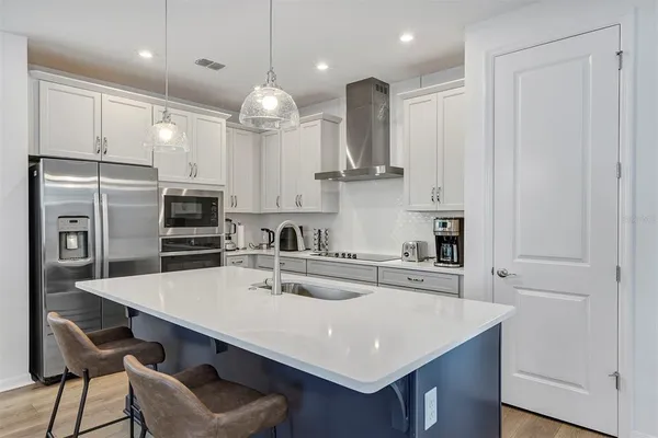 a kitchen with stainless steel appliances a sink a stove a refrigerator cabinets and chairs