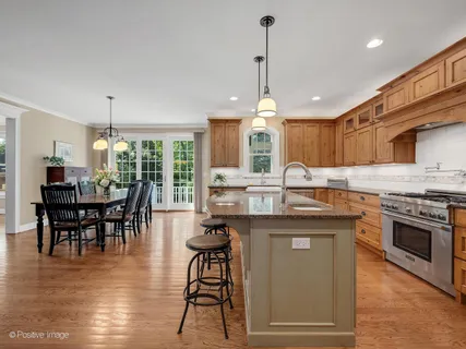 a kitchen with kitchen island granite countertop a stove a sink a dining table and chairs with wooden floor