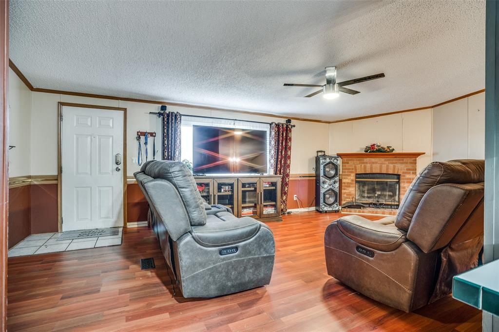 458 County Road 2131 Valley View, TX 76272 - Photo 3 of 13 Spacious living room featuring a brick wood-burning fireplace, ceiling fan, and crown molding. Vinyl flooring throughout, with ceramic tile at the entrance. Plenty of space to accommodate large couches for comfortable living