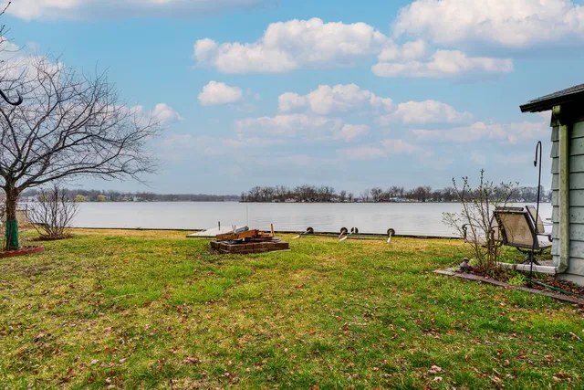 a view of a lake with lawn chairs and large trees