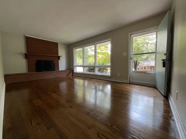 an empty room with wooden floor fireplace and windows