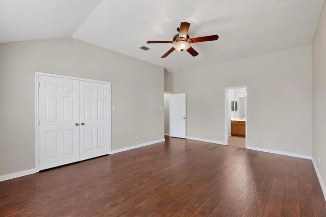 a view of an empty room with wooden floor and ceiling fan