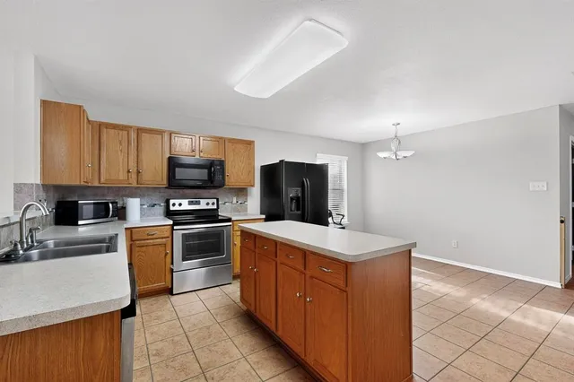 a kitchen with stainless steel appliances granite countertop a stove top oven a sink dishwasher and a refrigerator with wooden cabinets