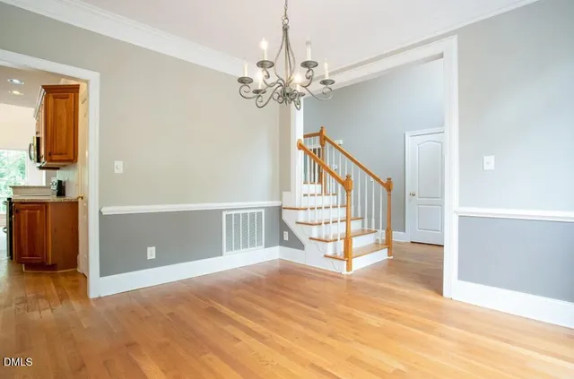 a view of an empty room with chandelier fan and wooden floor
