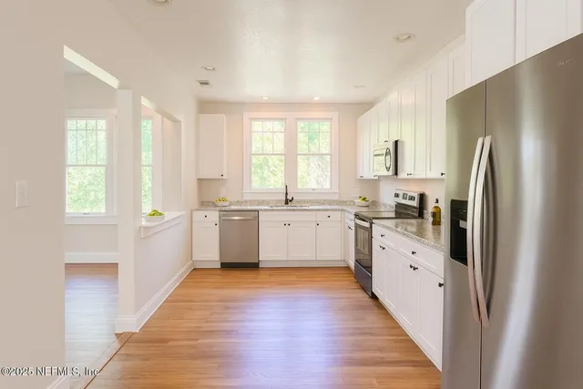a large kitchen with white cabinets and wooden floor