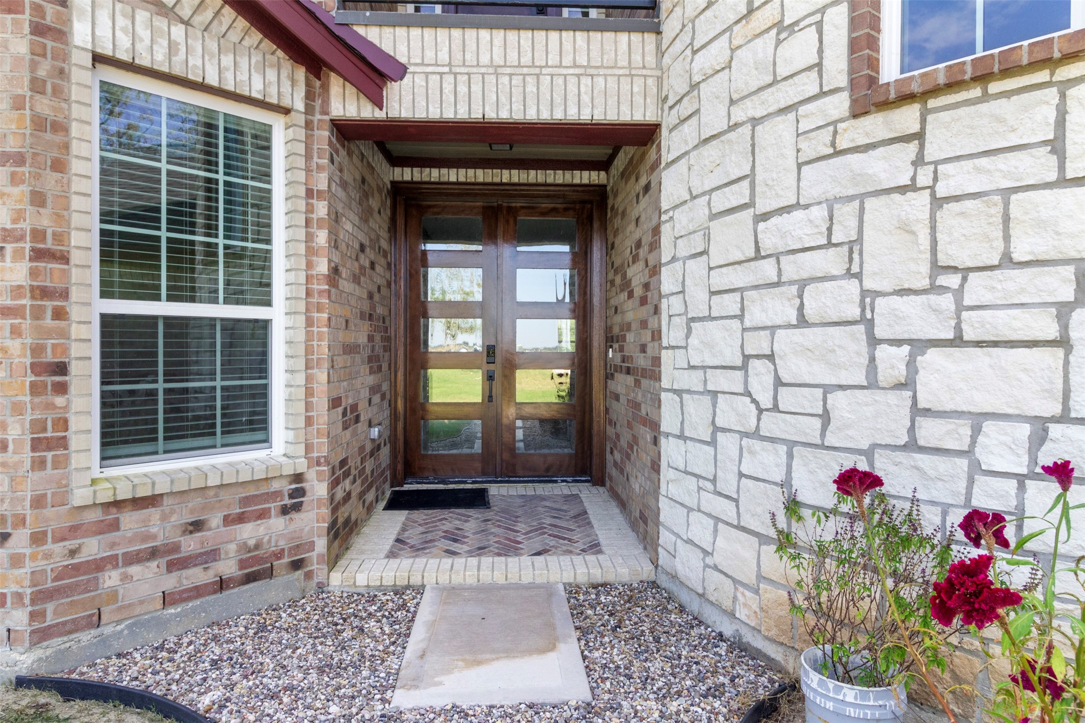 19920 County Road 647 Guy, TX 77444 - Photo 2 of 47 Charming entryway featuring a mix of brick and stone facade, double wooden doors, and a cozy porch with a herringbone-patterned walkway. A small garden area adds a touch of greenery.