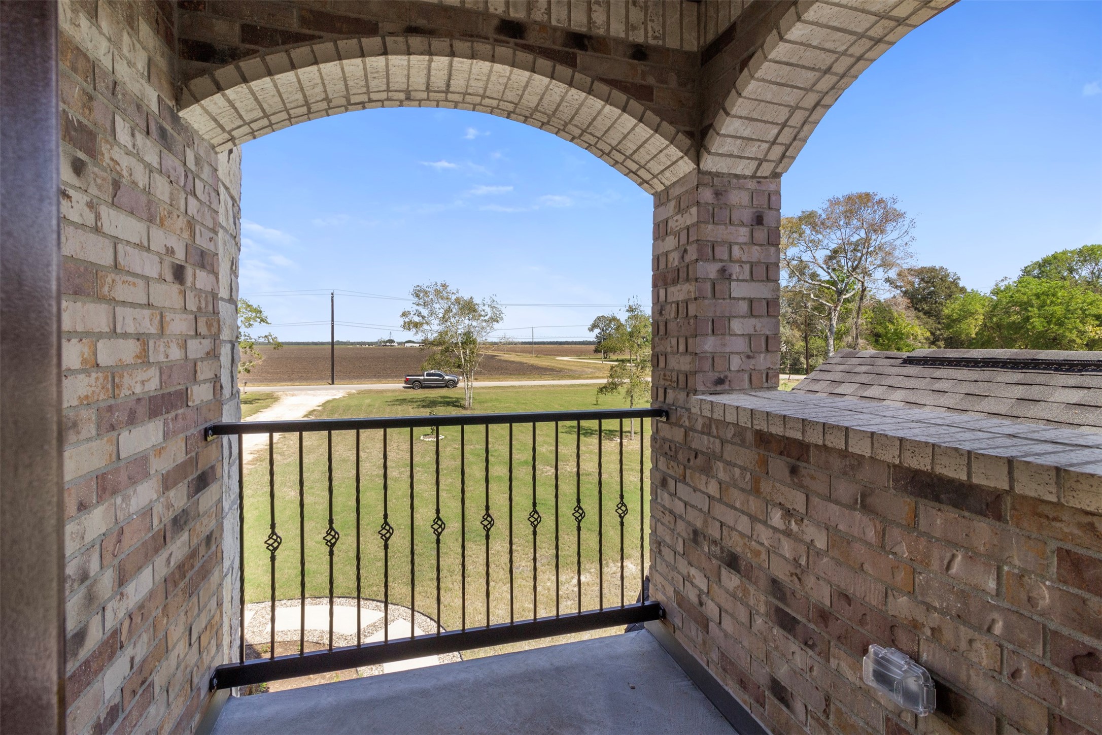 19920 County Road 647 Guy, TX 77444 - Photo 22 of 47 Charming brick balcony with a wrought iron railing offers scenic views of a spacious yard and open fields, perfect for enjoying peaceful countryside living.