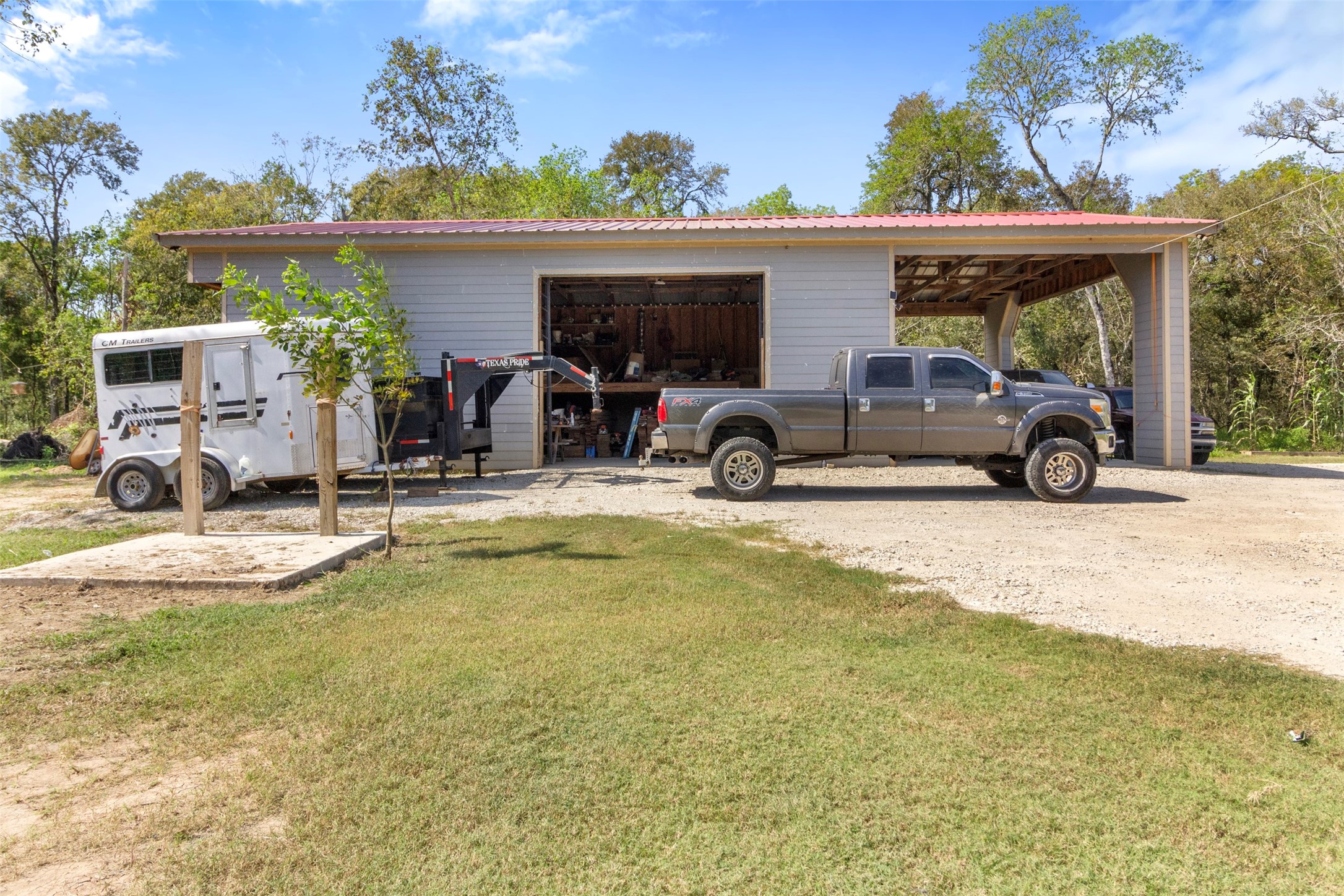 19920 County Road 647 Guy, TX 77444 - Photo 32 of 47 This photo shows a spacious garage or workshop with a large open door, a truck, and a trailer parked outside. It's set against a backdrop of trees, offering a practical and versatile space for various projects or storage needs.
