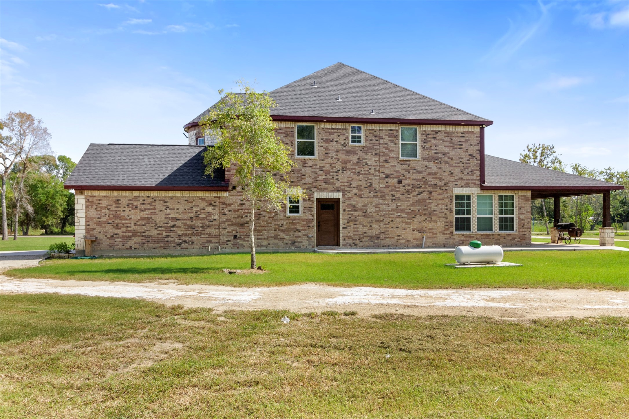 19920 County Road 647 Guy, TX 77444 - Photo 36 of 47 This photo showcases a two-story brick house with a spacious backyard. It features a well-maintained lawn, a small tree, and a covered patio area. The home is situated in a serene setting with ample outdoor space, ideal for privacy and relaxation.
