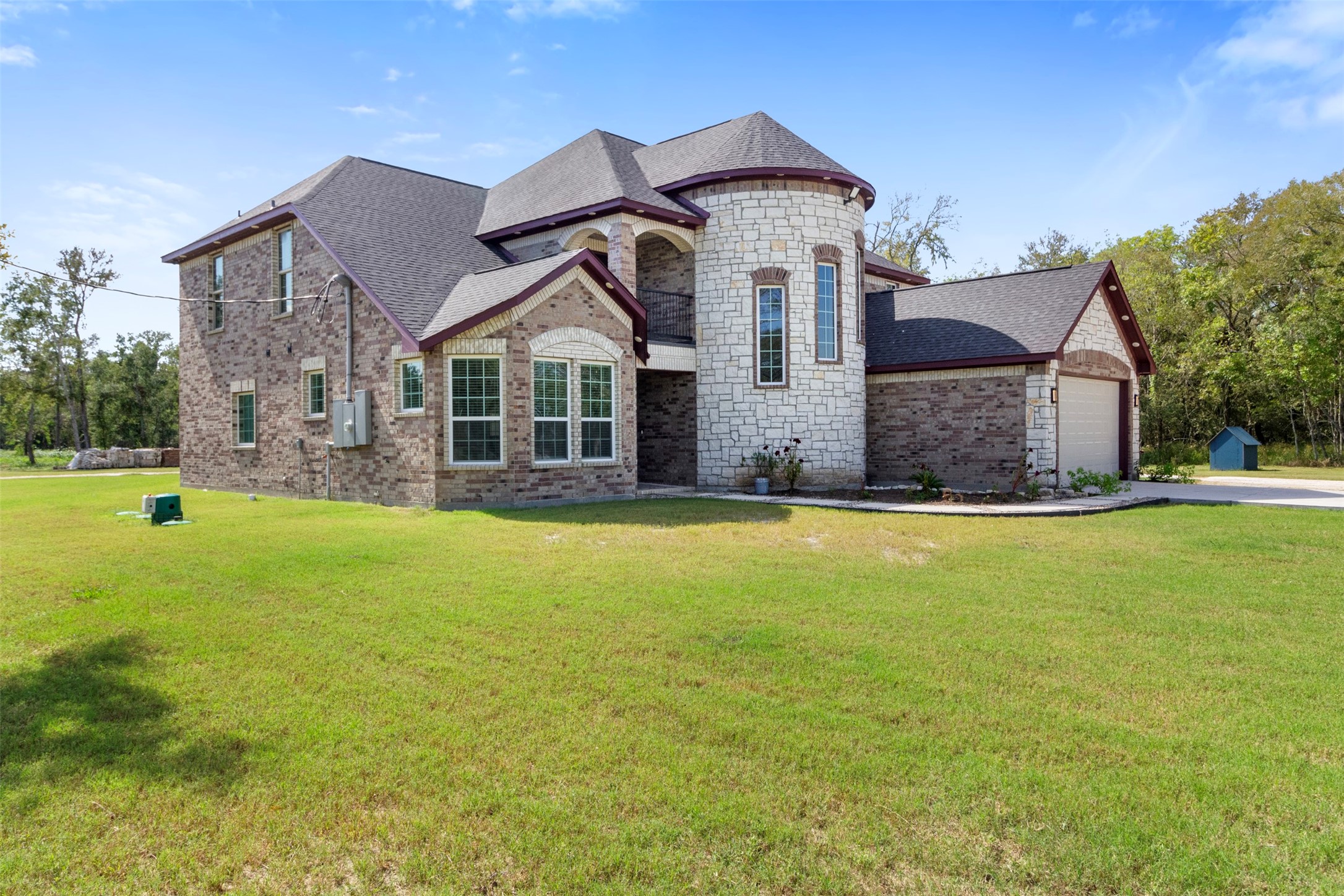 19920 County Road 647 Guy, TX 77444 - Photo 39 of 47 This is a spacious two-story home with a mix of brick and stone exterior, featuring a turret-like structure. It has a well-maintained lawn and a two-car garage, set in a scenic, wooded area.
