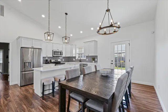 a kitchen with stainless steel appliances granite countertop a dining table chairs refrigerator and microwave